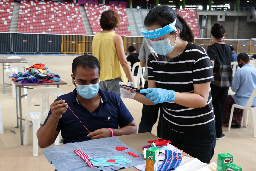 Representative of Singapore International Foundation, Ms Ng (on the right with a face shield) is joining the migrant workers in sewing. (Photo by Mulias)
