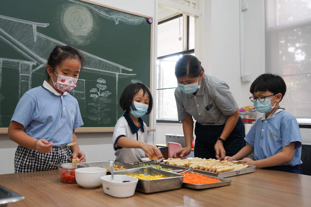 Students inserting the fillings of the Vegetarian Pita Sandwich under the watchful eye of Centre Manager Ms Lim Siew Lee. (Photo by Chan May Ching)